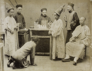 A man kneeling in front of the magistrate, with others wearing hats and carrying fans