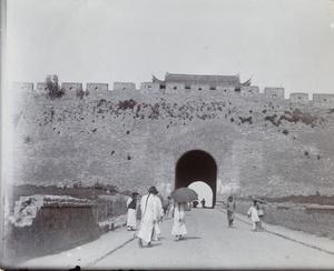 Pedestrians near a city wall and gate tower