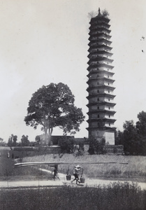 Porters carrying poles and pails past a pagoda