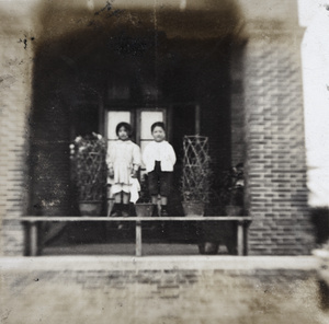 Maggie and Dick Hutchinson standing on a bench with potted plants on entrance verandah, 35 Tongshan Road, Hongkou, Shanghai