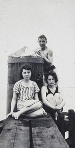 Two women and a man in bathing costumes on a wooden water pylon, Shanghai
