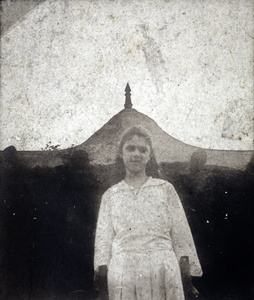 An unidentified woman in front of a thatched roof