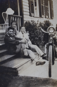 Three young people sitting on verandah steps and beside a motorcycle, Shanghai