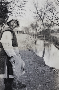An elderly woman beside a waterway holding a broom, Shanghai