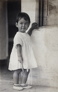 Bea Hutchinson holding a small shovel and standing on a summer house verandah, Moganshan