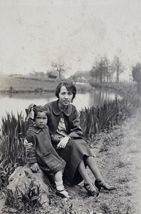 Unidentified woman and daughter sitting near a path beside a river, Shanghai