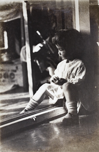 Bea Hutchinson gazing away from the photographer while sitting in a door frame, 35 Tongshan Road, Hongkou, Shanghai