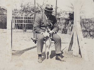 Charles Hutchinson sitting on a garden swing and holding up a dog standing on its hind legs, 35 Tongshan Road, Hongkou, Shanghai