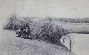 Fred Hutchinson holding a camera box, sitting with Sarah Hutchinson beside a park pond, Shanghai