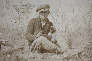 Harry Hutchinson wearing a newsboy cap and plucking feathers from a pheasant