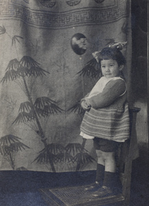 Bea Hutchinson, wearing a hand-knitted outfit, holding a balloon and standing on a chair, Shanghai