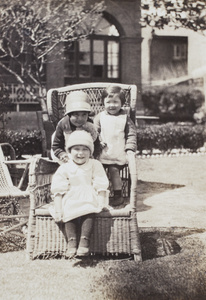 Cousins, Thelma Thiis, wearing a pom-pom hat, Bea Hutchinson, wearing a cloche hat, and Gladys Hutchinson, perching together on a garden chair, 35 Tongshan Road, Hongkou, Shanghai 