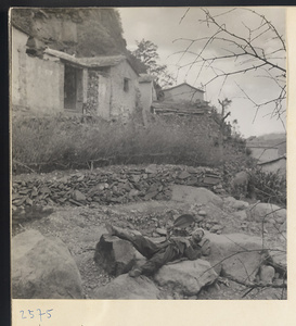 Houses, terraced walls, and man lying on rocks fanning himself in Tio-liu-po Village [sic]
