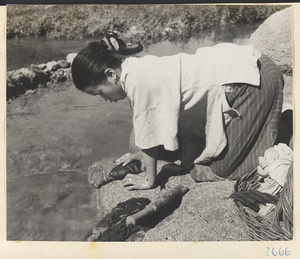Woman wearing a silver hair ornament with blue inlay work and washing clothes in a river in the Lost Tribe country