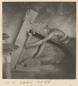 Man pressing wood pulp through a sieve at incense factory west of Ts'a-ho Village [sic] in the Lost Tribe country