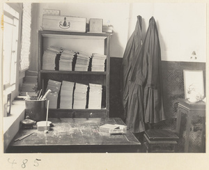 Room interior with table, books in bookshelf, and robes hanging from hooks
