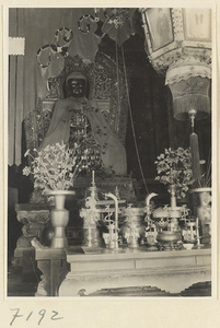 Interior of a temple building at Jie tai si showing an altar with draped statue of Buddha, ritual objects, and a lantern