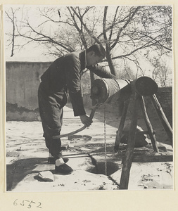 Man raising a bucket from a well with a hand crank