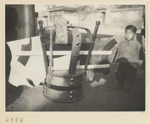 Boy standing next to itinerant shoe repairman's case and materials