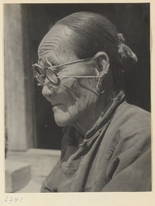 Woman, who makes souvenirs of braided colored straw, wearing eyeglasses, earrings, and hair ornament at Bei'anhe