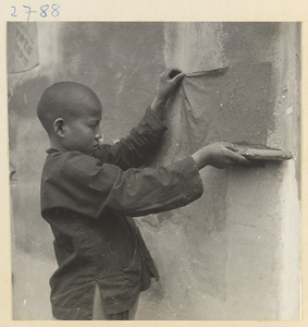 Boy hanging sheets of paper on a wall to dry outside paper-making shop