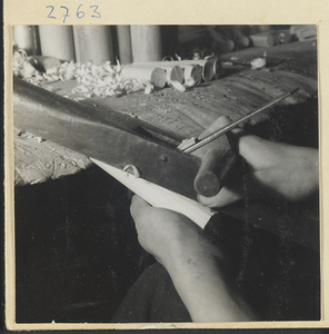 Man hand-planing the wooden body of a stringed instrument in a workshop