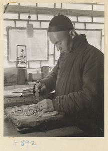 Man hammering a design into a metal sheet in a workshop that makes iron pictures