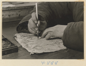 Man inking a design onto a piece of paper in a workshop that makes iron pictures