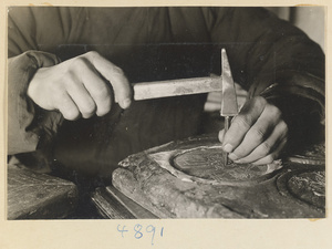 Man hammering a design into a metal sheet in a workshop that makes iron pictures