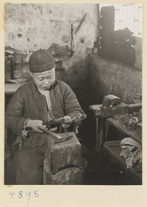 Boy using a hammer and tongs to bring out the relief work in a workshop that makes iron pictures