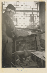 Man using a press in a workshop that makes iron pictures