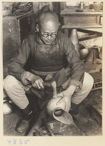 Coppersmith hammering a pitcher in a workshop