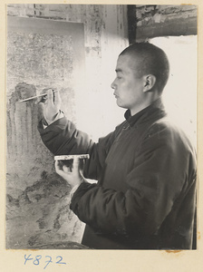 Man in a scroll-mounting shop retouching a scroll painting on a drying board called a zhuang ban