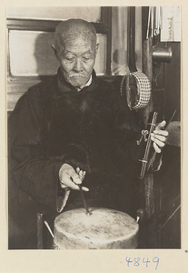 Musician with drum, castanets, and stringed instrument accompanying a shadow-puppet performance