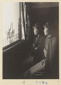 Two women watching a shadow-puppet performance of two figures in a boat