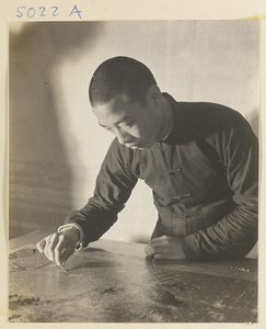 Interior of a scroll-mounting shop showing a man using iron tweezers to remove bits of the old paper backing from a scroll painting