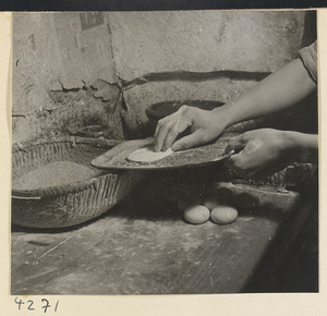 Kitchen interior showing a man coating dough with sesame seeds to make ma bing