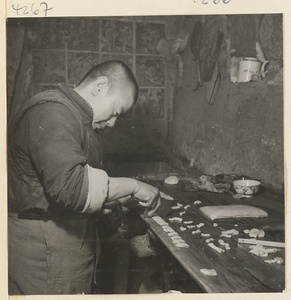Kitchen interior showing a man cutting dough into pieces to make oil cakes