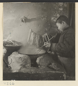 Kitchen interior showing a boy frying oil cakes in a wok