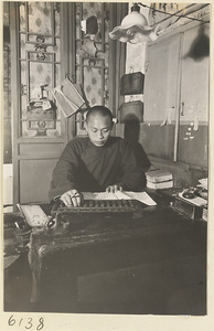 Grain merchant at a desk calculating with an abacus and writing in an acount book