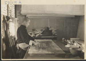 Interior of a scroll-mounting shop showing a man using a soft paste brush to apply paste to the backing of a scroll painting