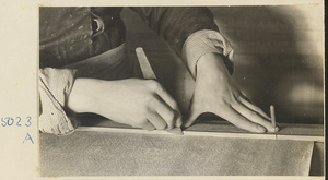 Interior of a scroll-mounting shop showing a man trimming the edge of a scroll with a steel paper knife