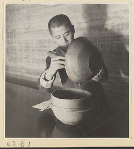 Interior of a scroll-mounting shop showing a man pouring thinned paste called hu or jiang hu into a horsehair strainer