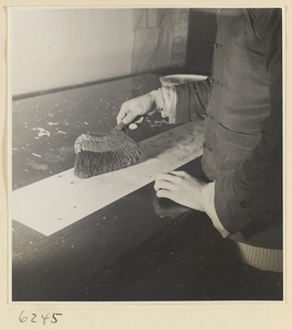 Interior of a scroll-mounting shop showing a man using a brush to steady a scroll painting while removing the old paper backing