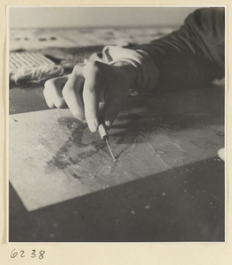 Interior of a scroll-mounting shop showing a man using a steel needle to remove the old backing from a scroll painting