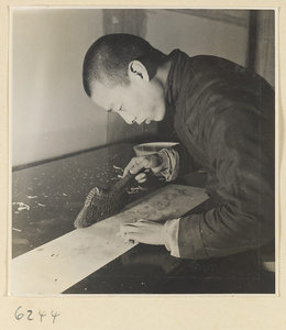 Interior of a scroll-mounting shop showing a man using a brush to steady a scroll painting while removing the old paper backing
