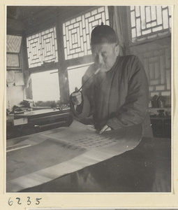 Interior of a scroll-mounting shop showing a man smoking a pipe and looking at a scroll painting with an inscription