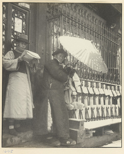 Newsstand with man reading a paper and man holding a parasol