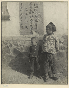 Two children standing in front of a notice affixed to a building