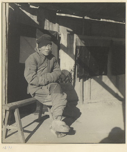 Person dressed in winter clothes seated on a sawhorse outdoors in the sun